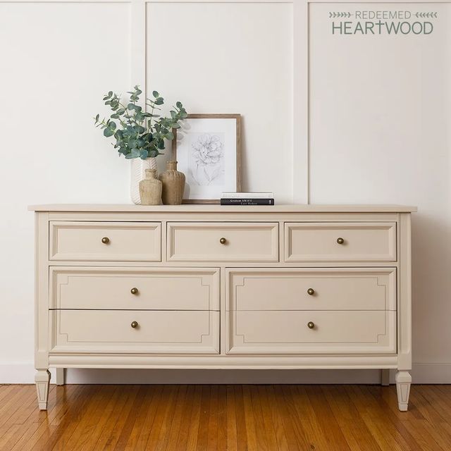 a white dresser sitting on top of a hard wood floor next to a vase with a plant