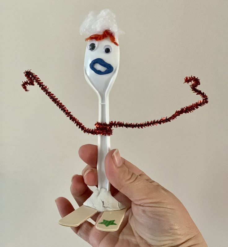 a hand holding a plastic spoon with a face on it and a string attached to it