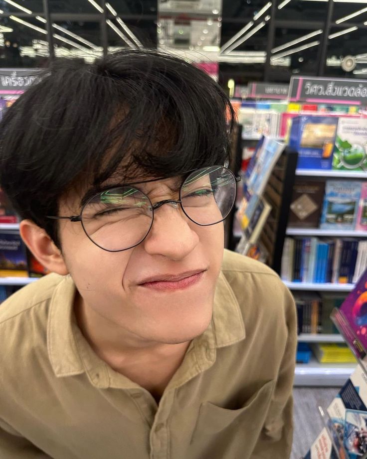 a man wearing glasses and looking at the camera in a store aisle with bookshelves behind him