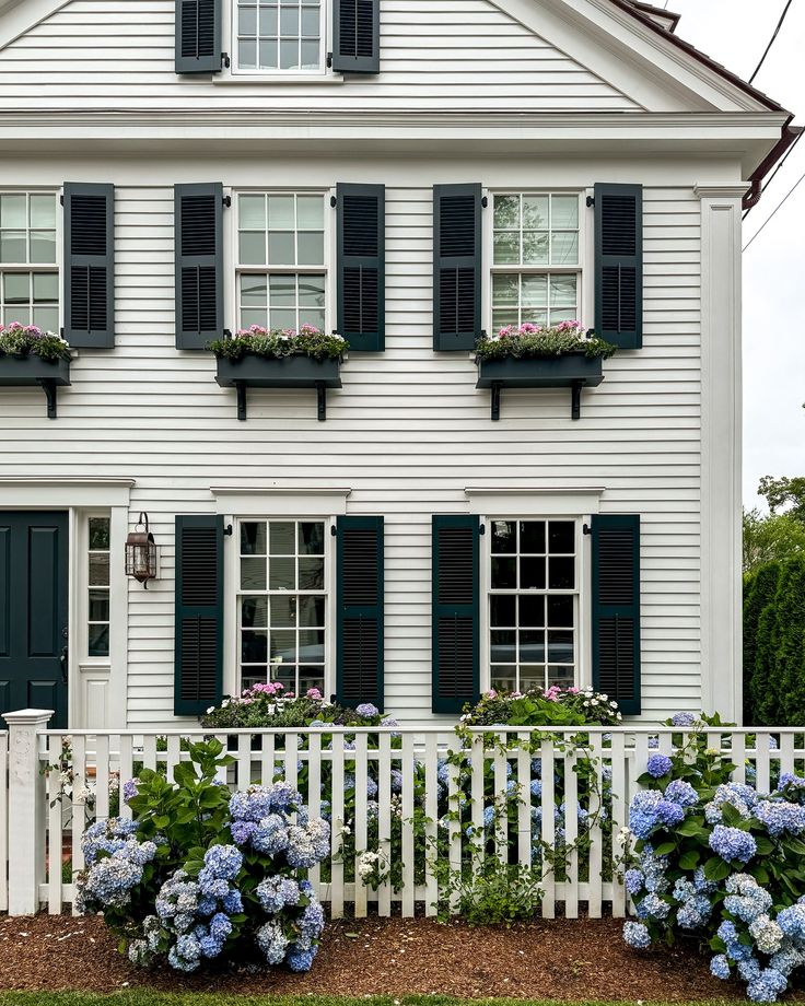 a white house with green shutters and blue flowers