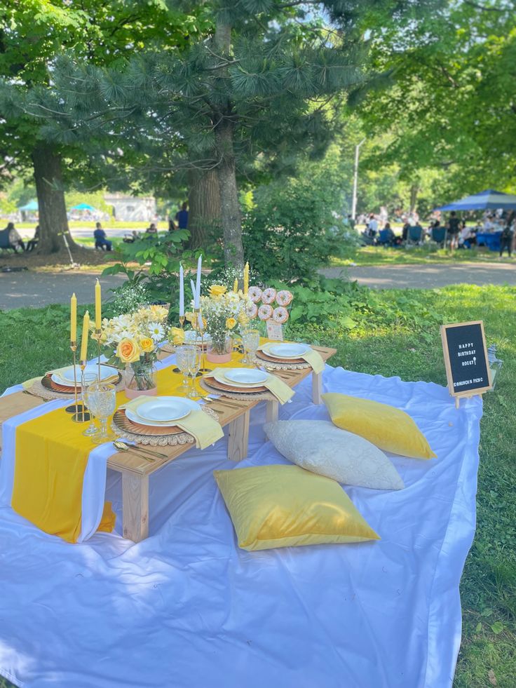 a table set up with yellow and white linens for a picnic in the park