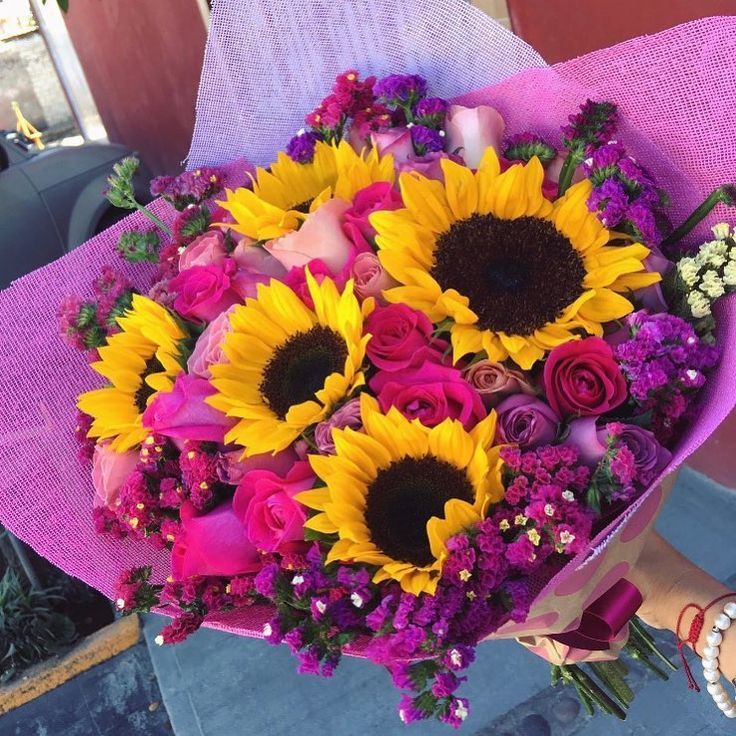 a bouquet of sunflowers and roses is held by a woman