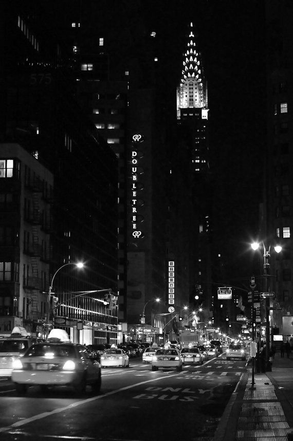 a city street at night with cars driving on the road and tall buildings in the background