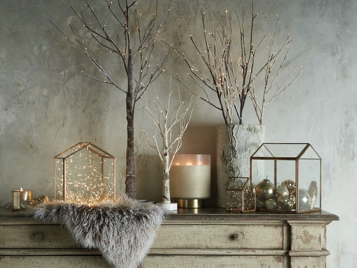 a mantle with candles, branches and other decorative items on it in front of a gray wall