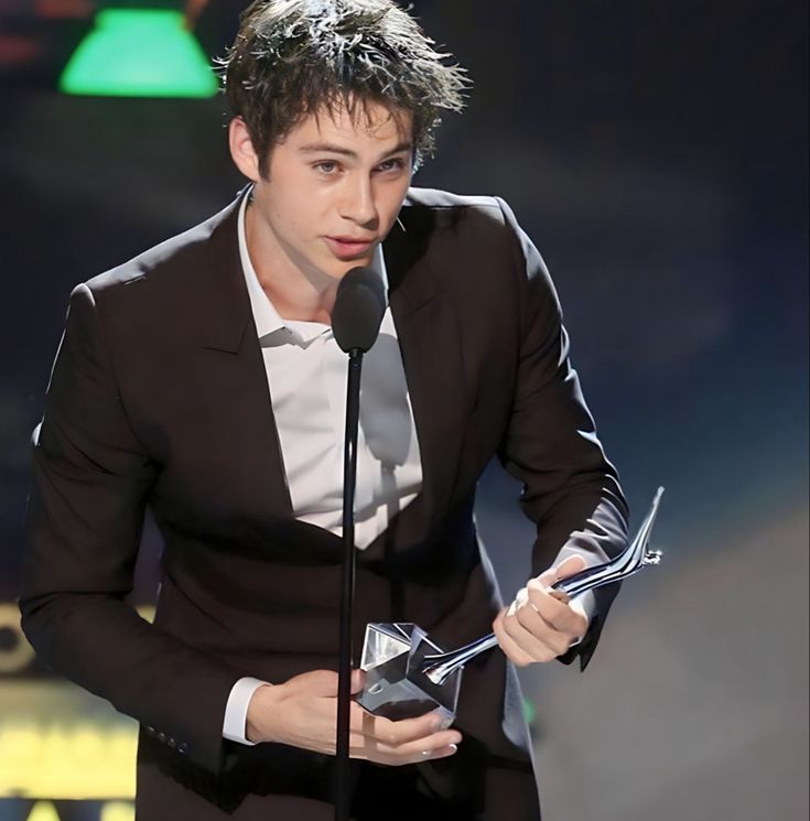 the young man is holding an award in front of a microphone and wearing a suit