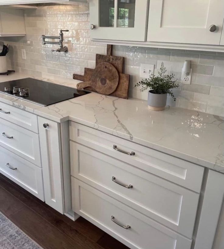 a kitchen with white cabinets and marble counter tops