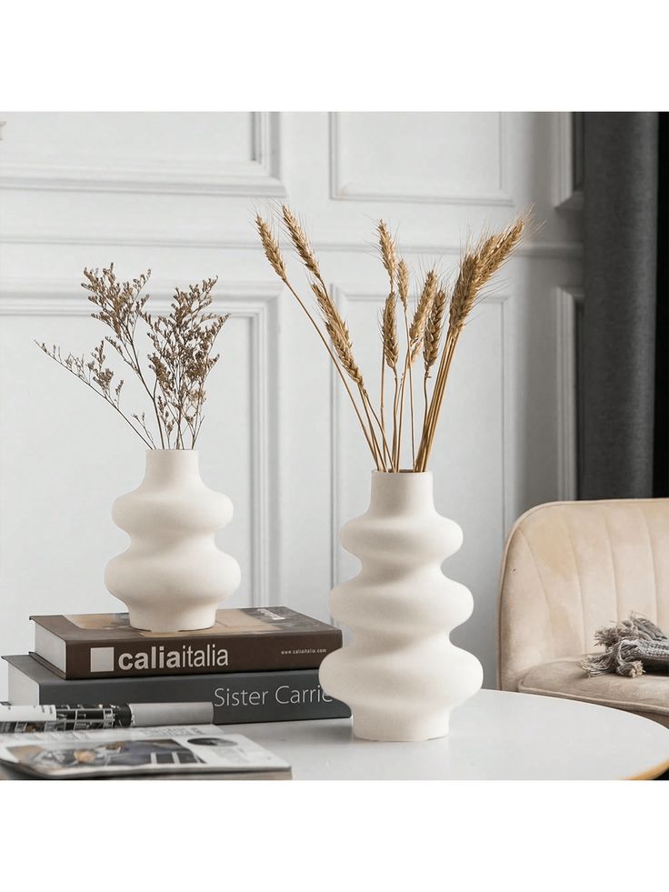 two white vases sitting on top of a table next to books and a chair