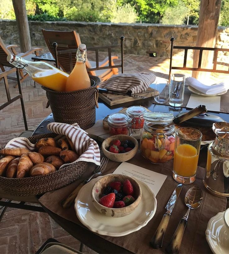 the table is set for breakfast outside on the patio with fruit, juice and bread