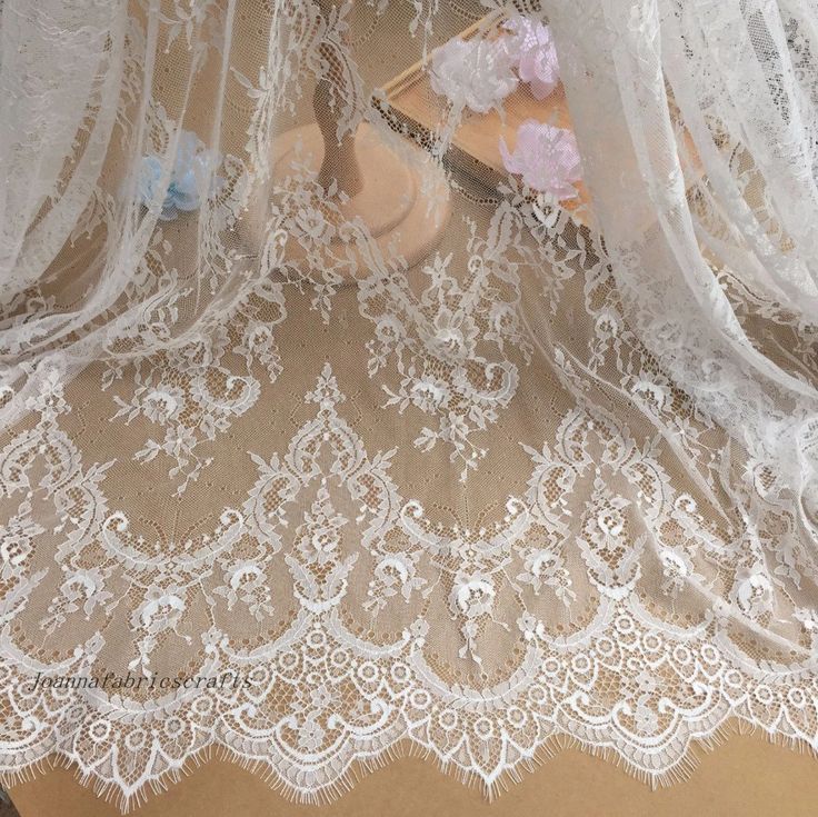 white lace with pink flowers on it sitting on top of a wooden table next to a vase