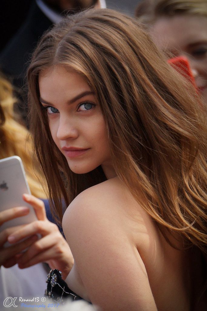 a young woman looking at her cell phone while sitting in front of other people with long hair