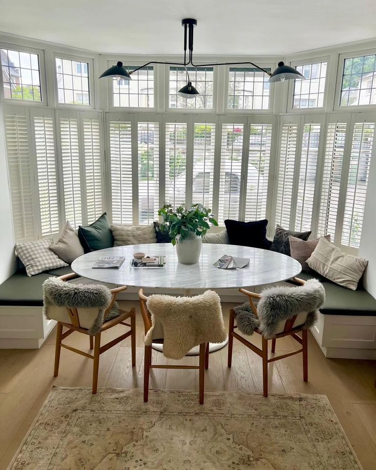 a dining room table with four chairs and a bench in front of the bay window