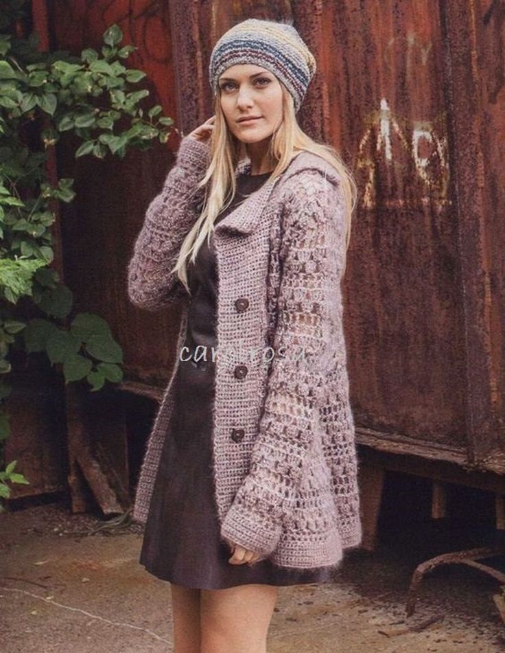 a woman wearing a knitted coat and hat standing in front of a rusty building