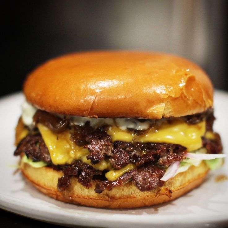 a cheeseburger with meat and onions on a white plate