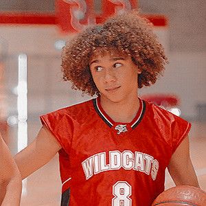 a young man holding a basketball while standing next to another person in a red uniform