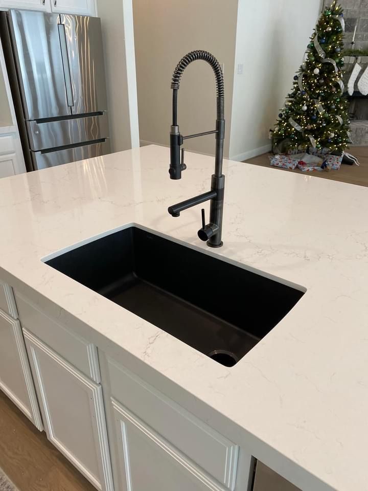 a kitchen sink sitting under a faucet next to a counter top with a christmas tree in the background