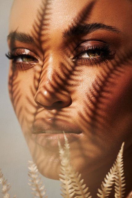 a woman's face is shown through the shadow of plants and leaves on her face