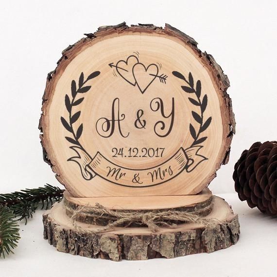 a wooden slice with the initials and date engraved on it, next to pine cones