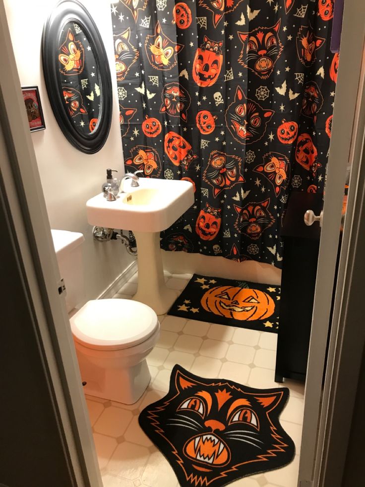 a bathroom decorated for halloween with black and orange shower curtain, white toilet and sink