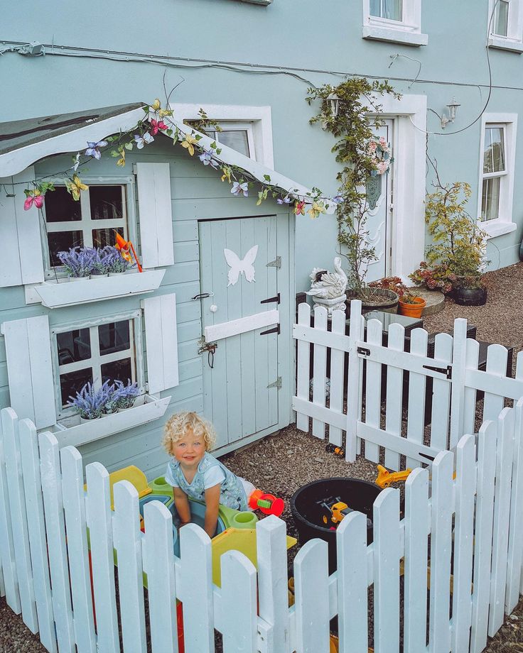 a little boy sitting in a toy house made out of wooden picket fence and flowers