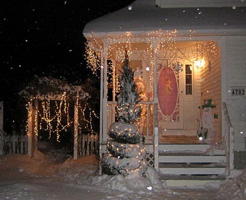 a house covered in snow with christmas lights on it's porch and front door