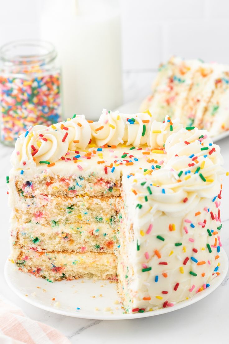 a cake with white frosting and sprinkles is cut in half on a plate