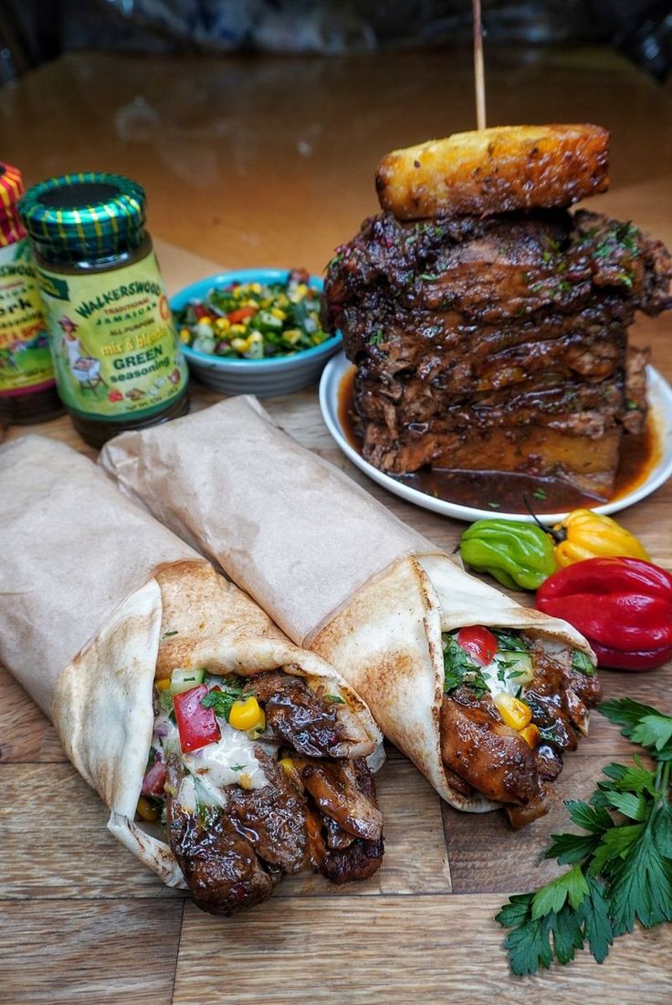 two burritos with meat and vegetables on a table next to condiments