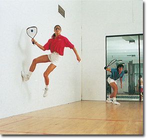 a woman jumping in the air with a tennis racquet while another man watches