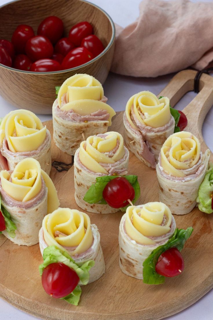 small sandwiches with cheese and tomatoes on a cutting board next to a bowl of cherries