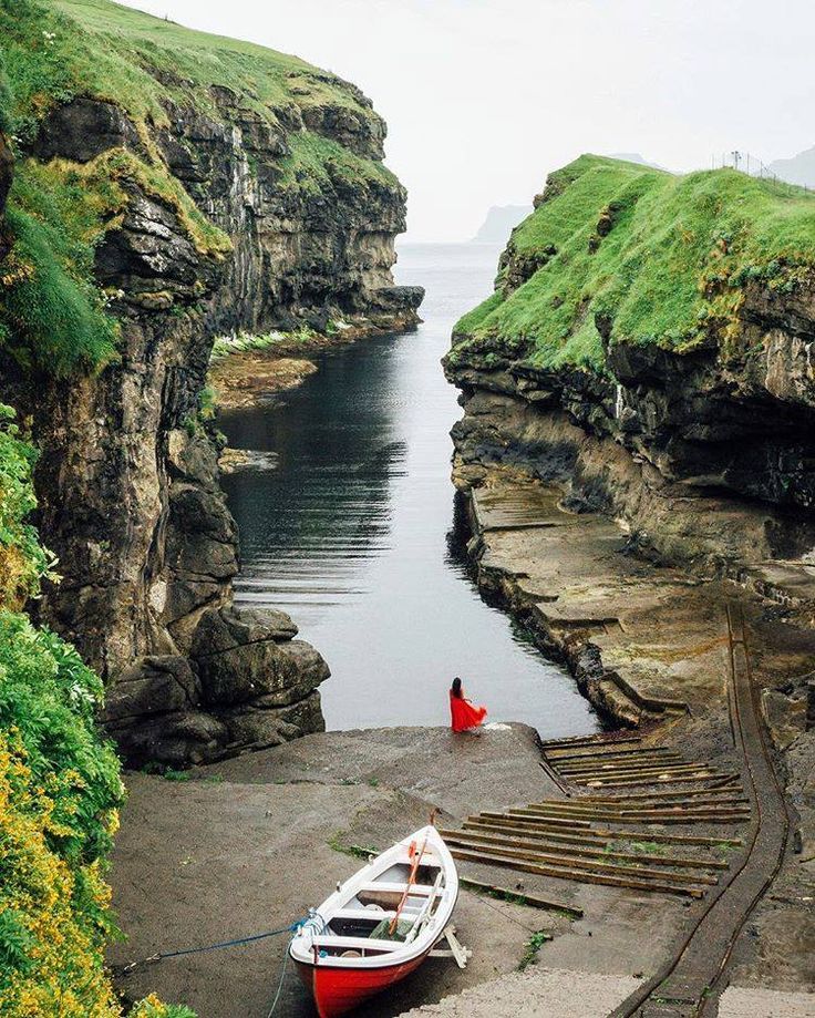 there is a small boat that is docked at the edge of the water near some cliffs