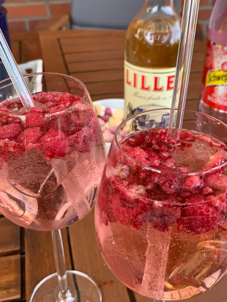 two glasses filled with ice and raspberries on a table