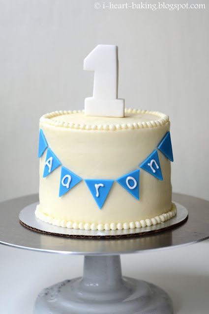 a birthday cake with the number one on it and bunting around the top is white frosting