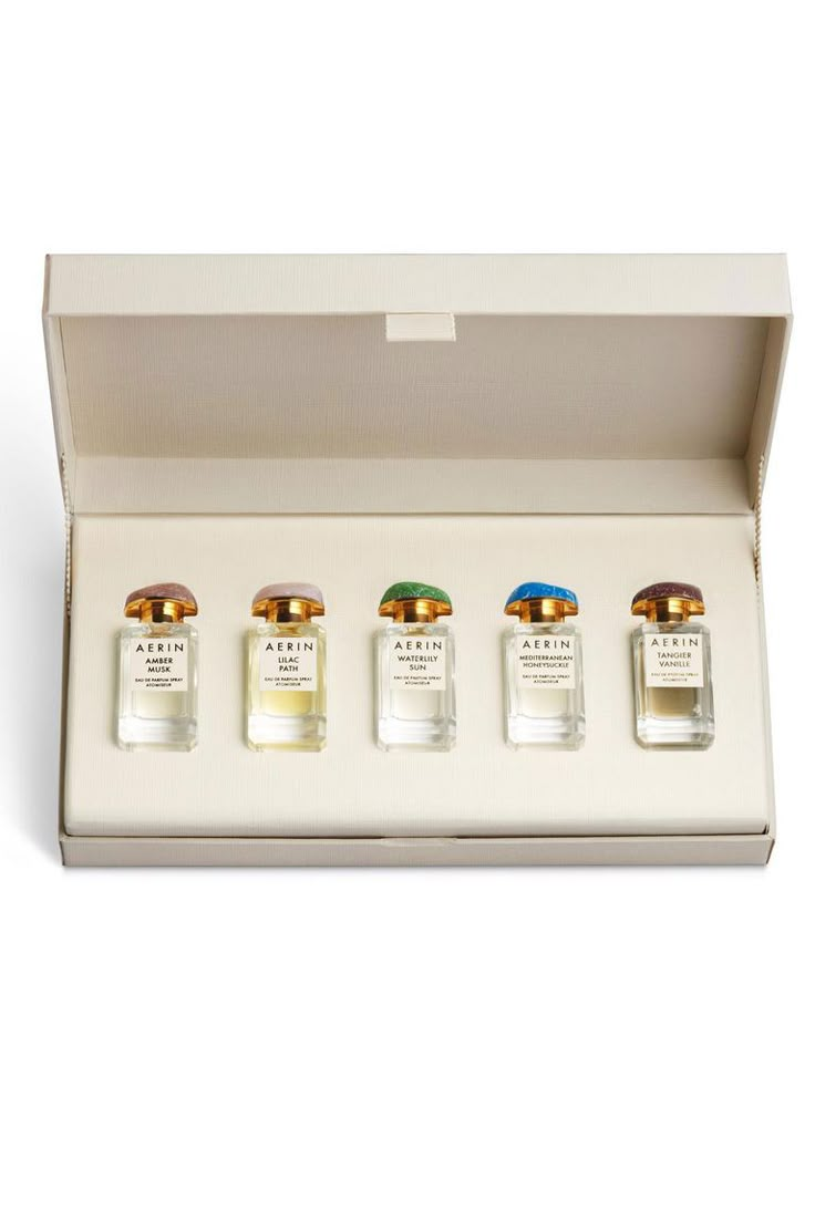 four bottles of perfume in a white box on a white surface with the lid open