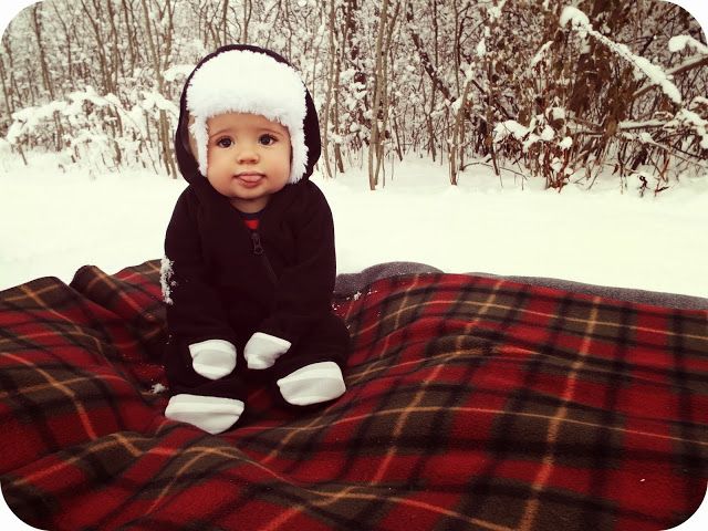 a baby is sitting on a blanket in the snow wearing a hat and mittens