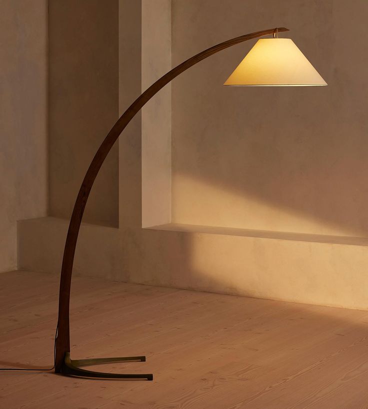 a floor lamp with a white shade on it in an empty room next to a wall