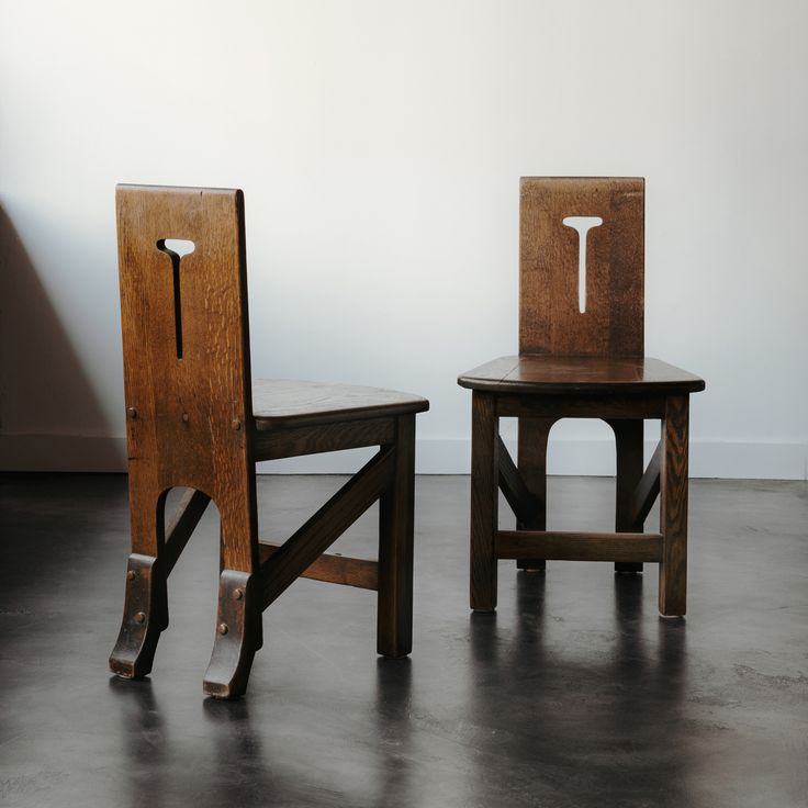 two wooden chairs sitting next to each other on top of a cement floor in front of a white wall