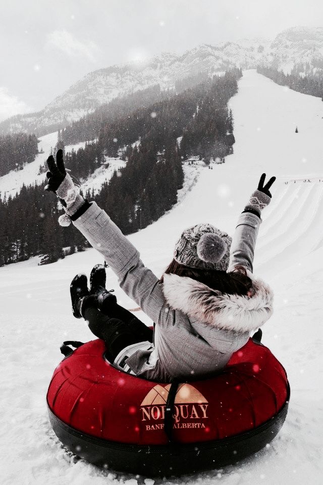 a woman is sitting on top of a tube in the snow with her arms up