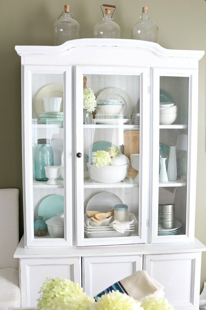 a white china cabinet filled with dishes and flowers