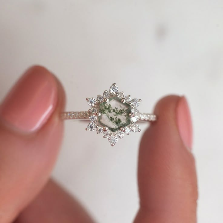 a woman's hand holding a ring with a green stone surrounded by diamonds on it