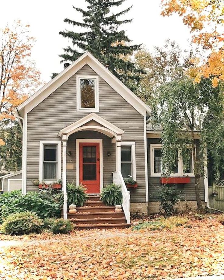 a gray house with red front door and steps leading up to the entryway is surrounded by fall foliage