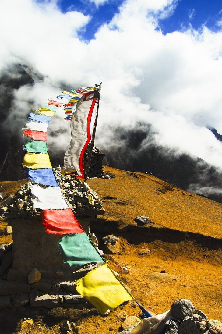 colorful flags are hanging on the side of a mountain with clouds in the sky behind them