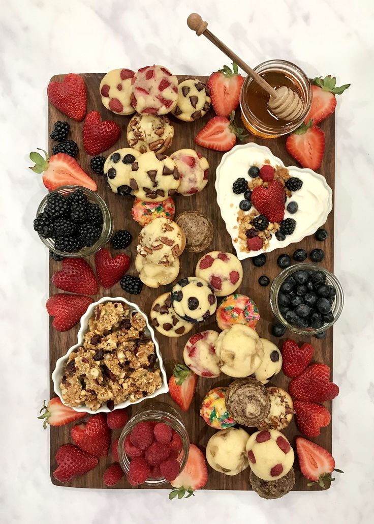 a wooden tray topped with muffins covered in toppings next to berries and strawberries