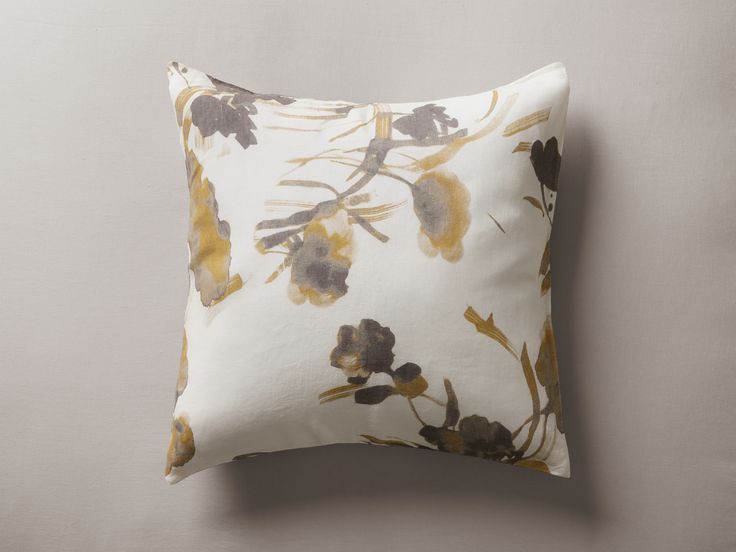 a white pillow with yellow and grey flowers on it, against a gray wall background