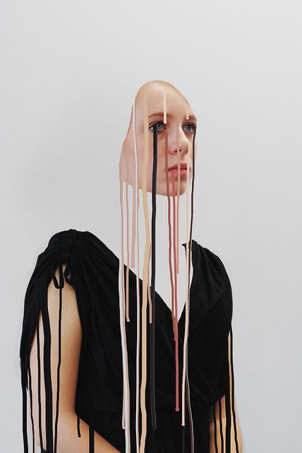 a woman with long hair and dripping paint on her face is standing in front of a white wall