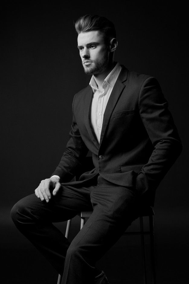 a man in a suit is sitting on a chair and posing for a black and white photo