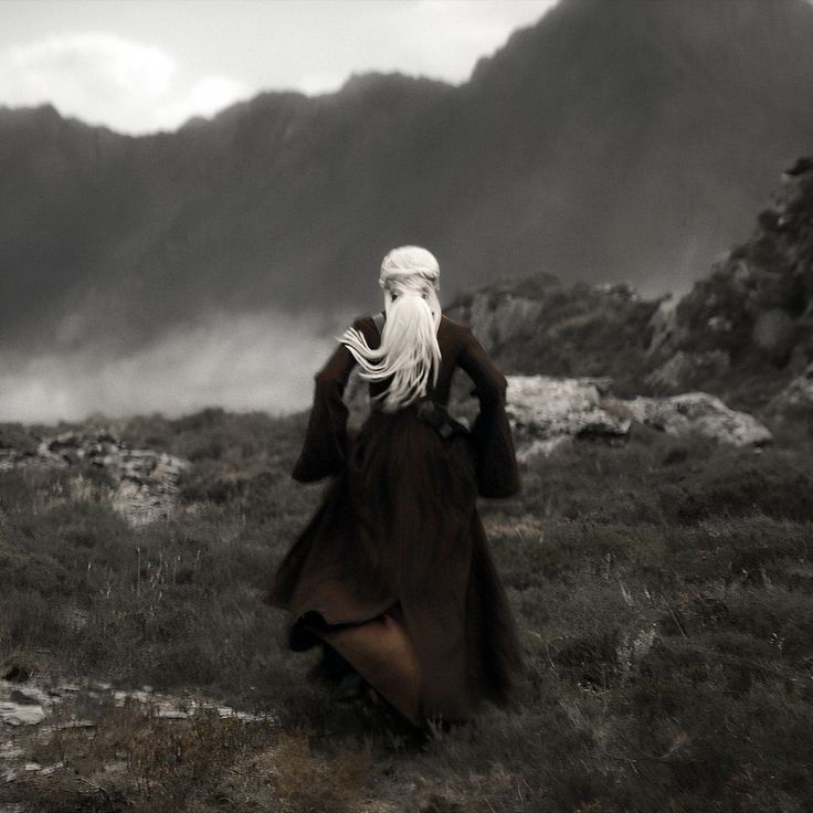 a man with long white hair is walking in the mountains