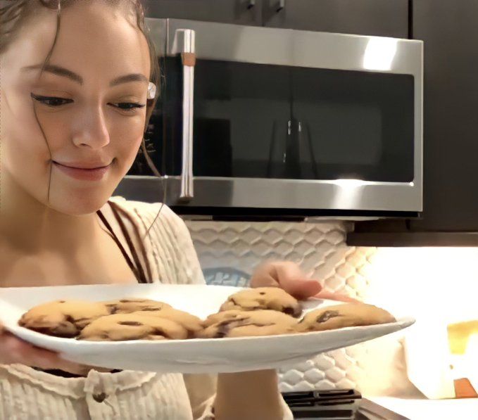 a woman holding a plate with chocolate chip cookies on it in front of a microwave