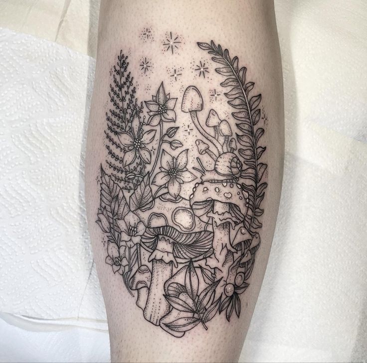 a black and white photo of a tattoo on the leg with flowers, leaves and mushrooms