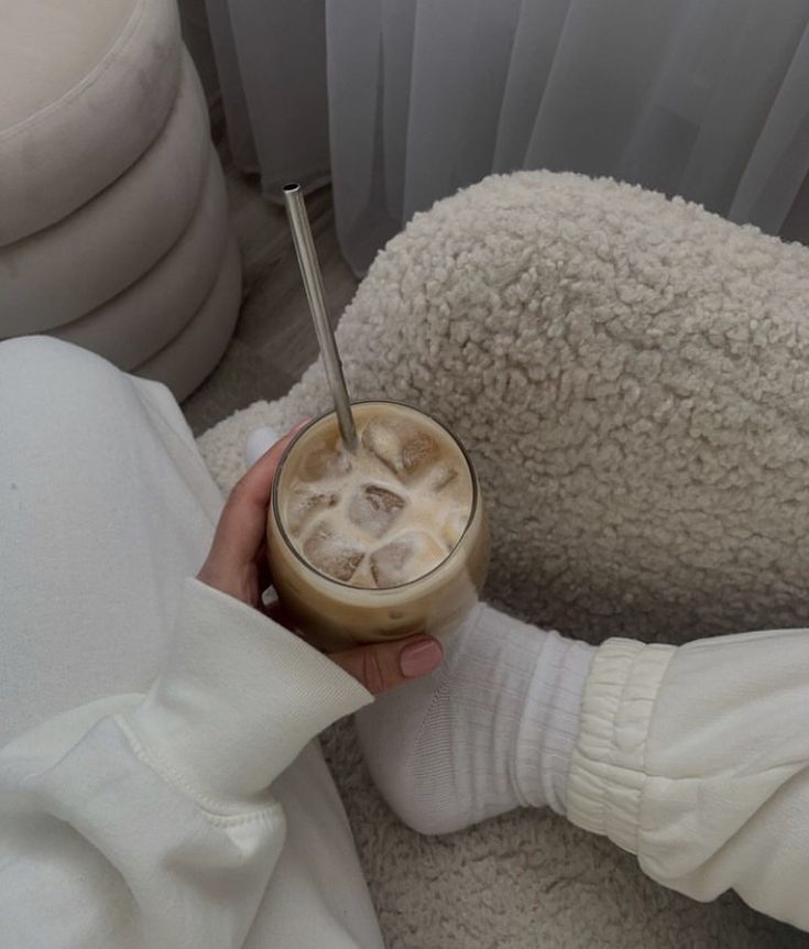 a person is holding a drink in their hand while sitting on a fluffy white chair