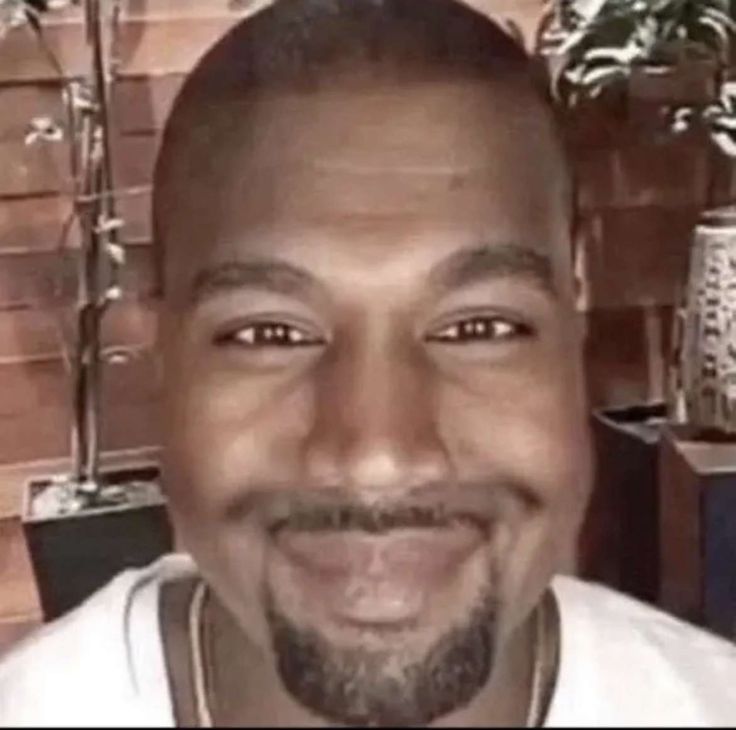 a close up of a person wearing a white shirt and smiling at the camera with plants in the background