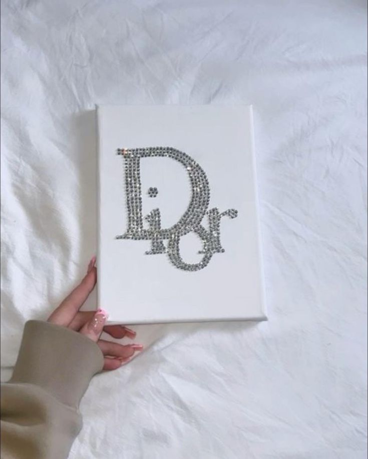 a person holding up a book with the letter d on it's cover, which is decorated with swarong crystals